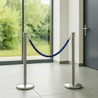 Two silver stanchions with blue rope in front of a glass door with a view of greenery.