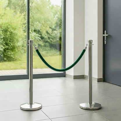 Two silver stanchions with green rope in front of a glass door with a view of greenery.